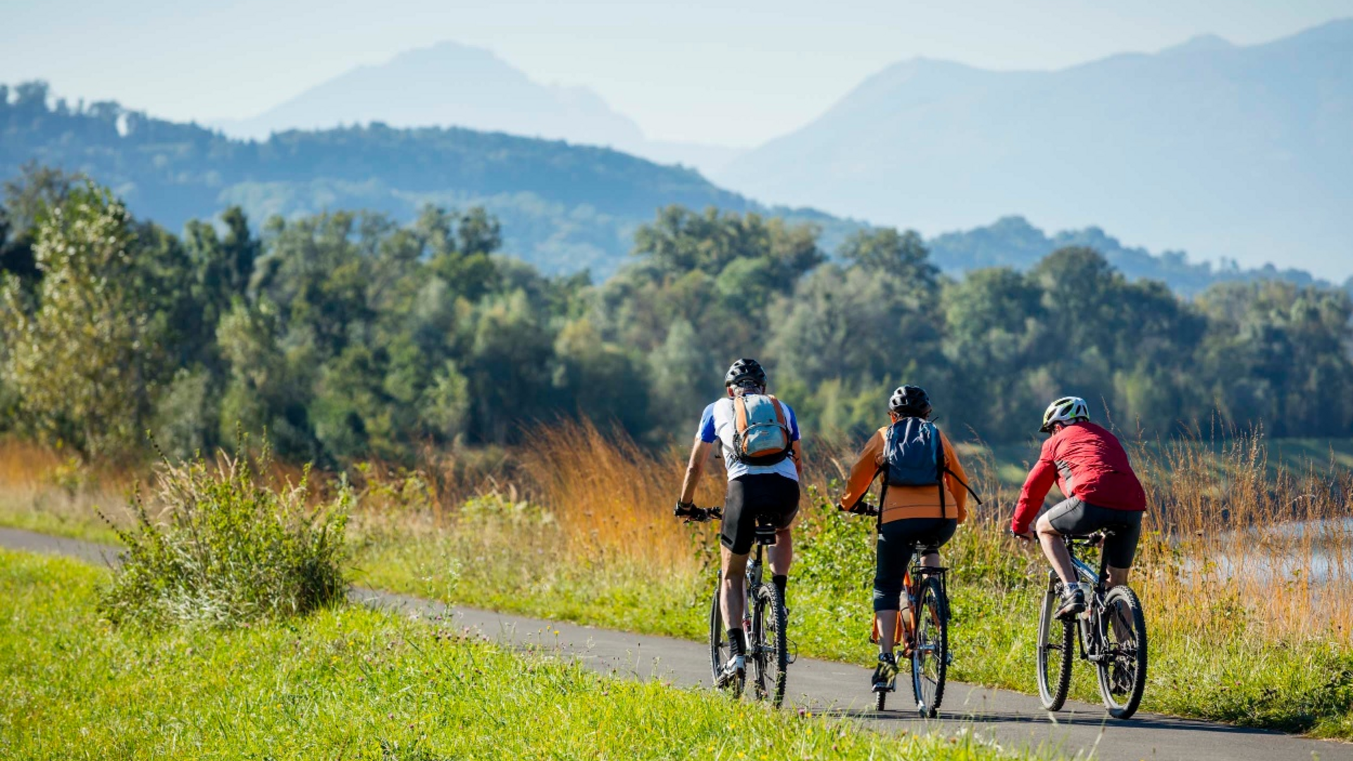 Three cyclists riding on a path through nature with mountains in the background
