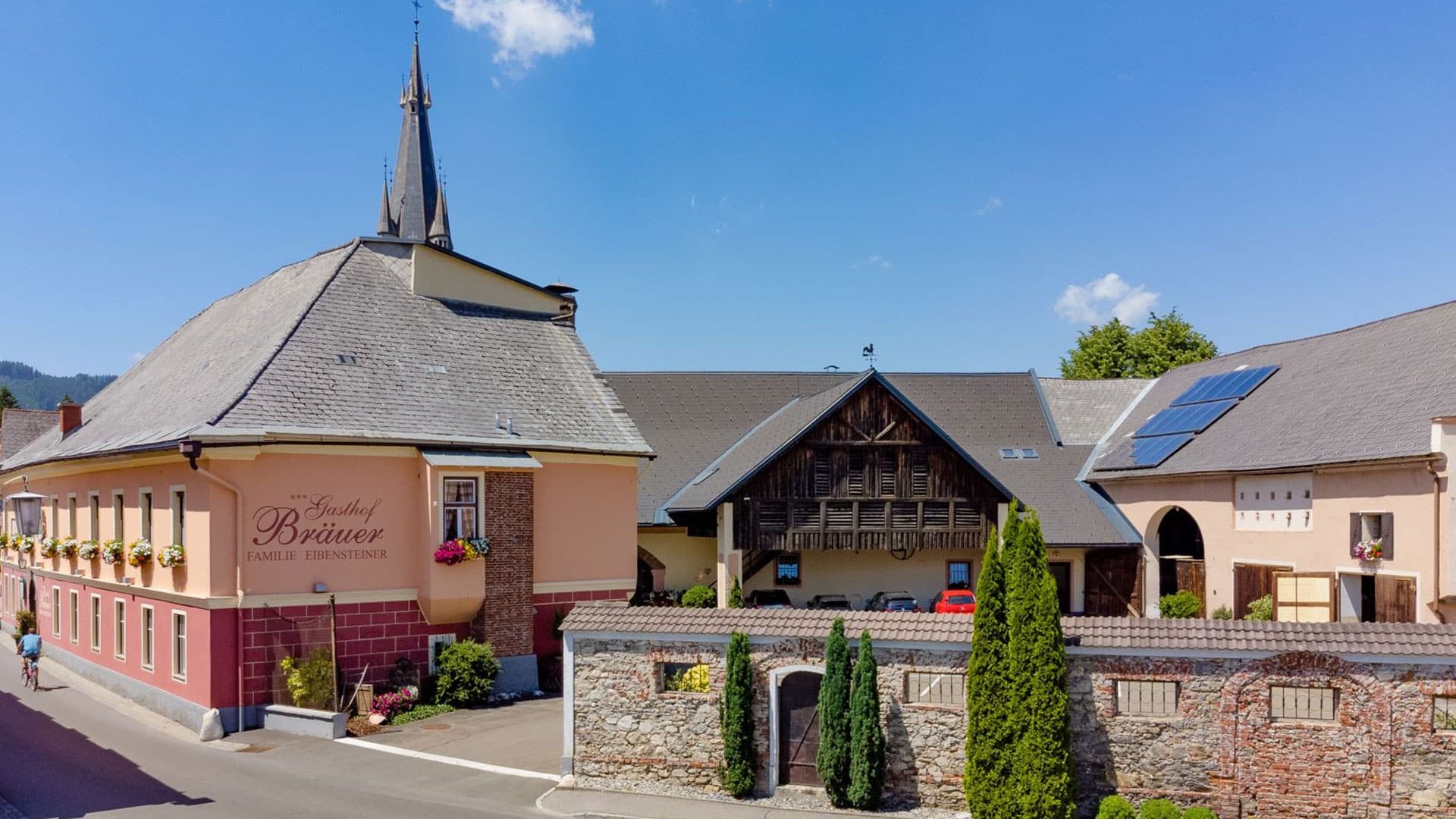 Inn Bräuer with pointed church tower, stone wall, and blue sky