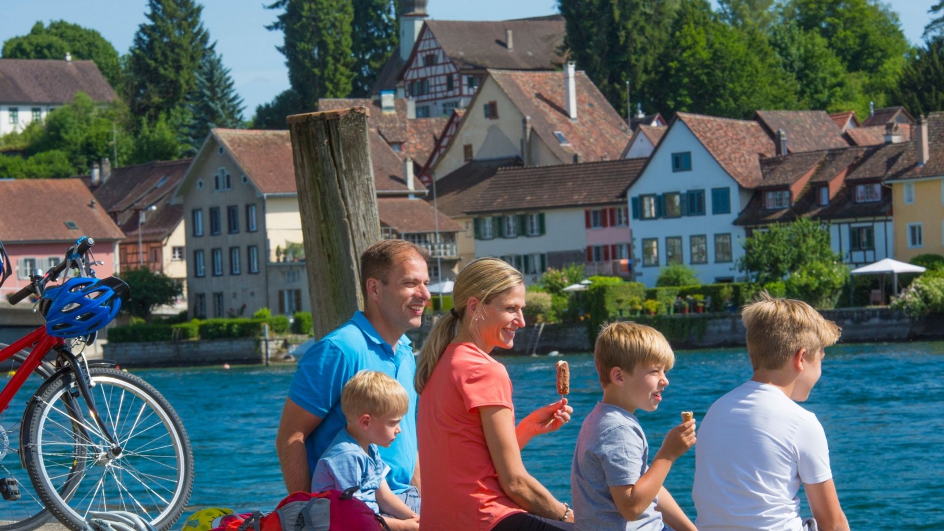 Family sitting by water eating ice cream in front of picturesque houses in summer