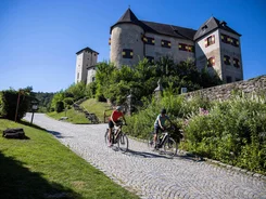 Zwei Radfahrer vor einem alten Schloss auf Kopfsteinpflasterstraße bei Sonnenschein