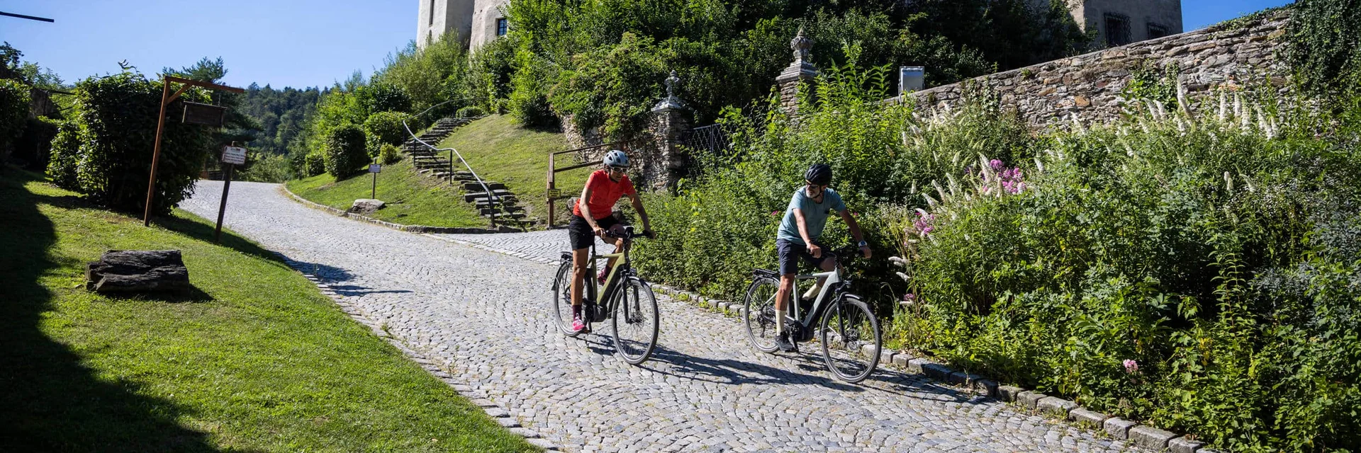 Twee fietsers op een geplaveide weg met een historisch kasteel op de achtergrond