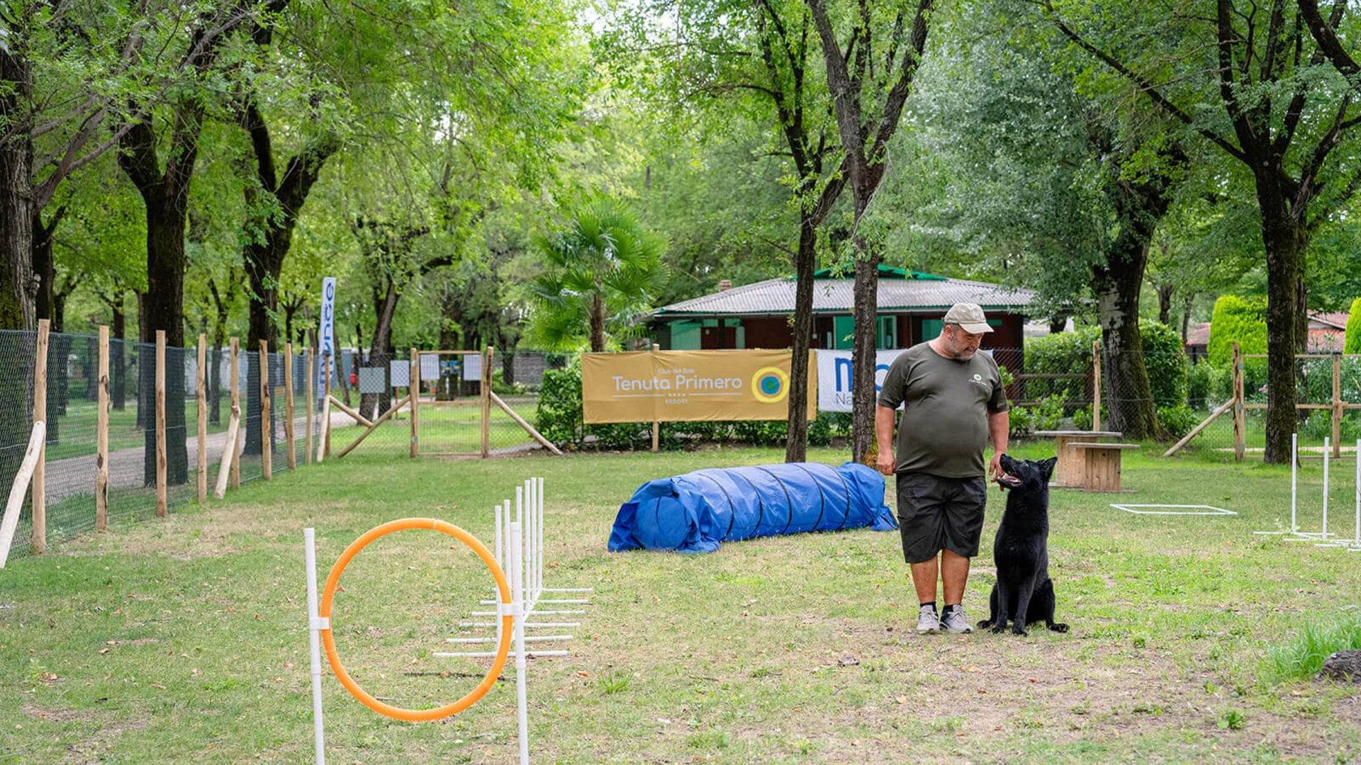 Man training black dog in outdoor agility course