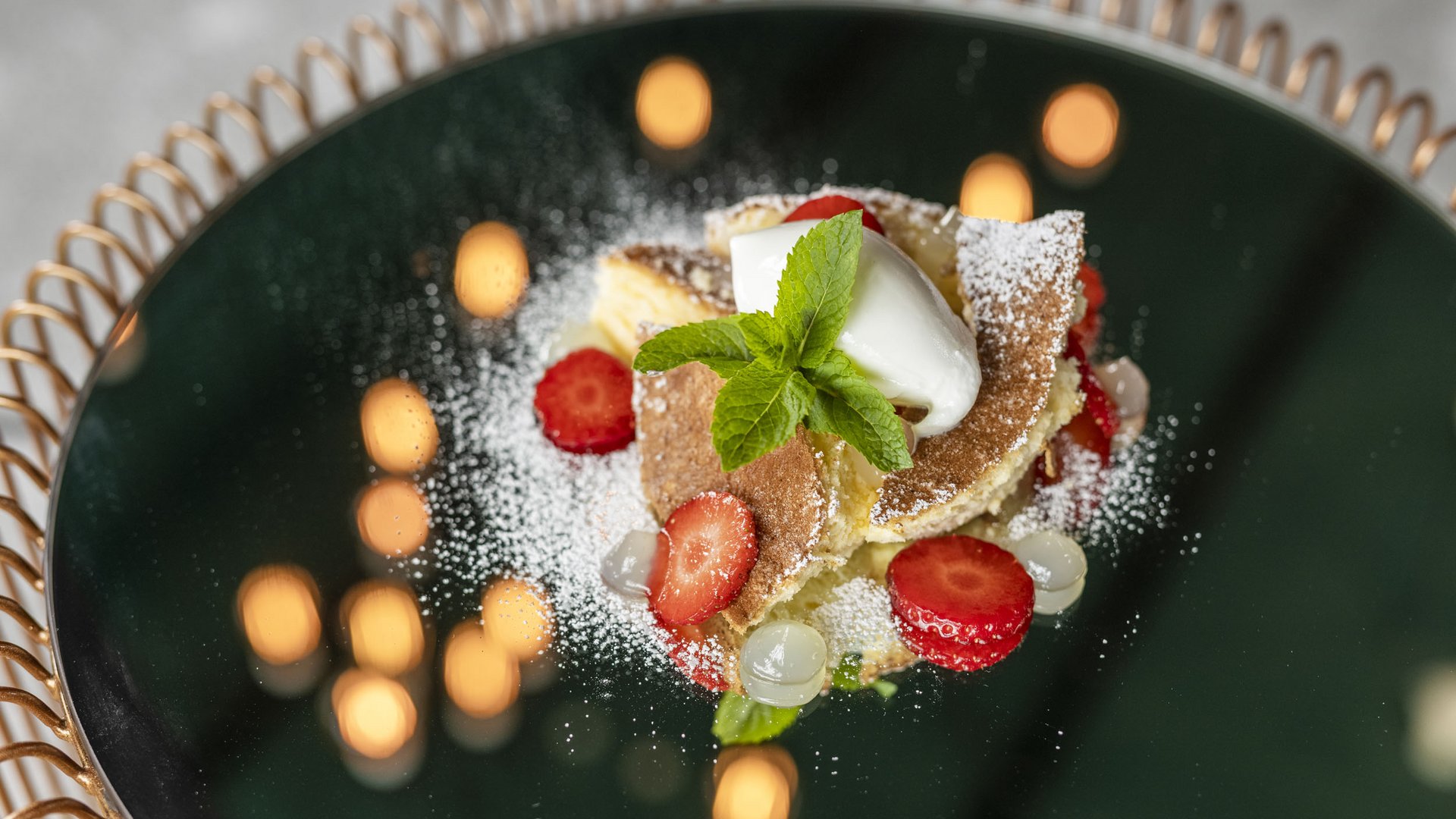 Dessert with sponge cake, strawberries, mint, and powdered sugar on black mirror
