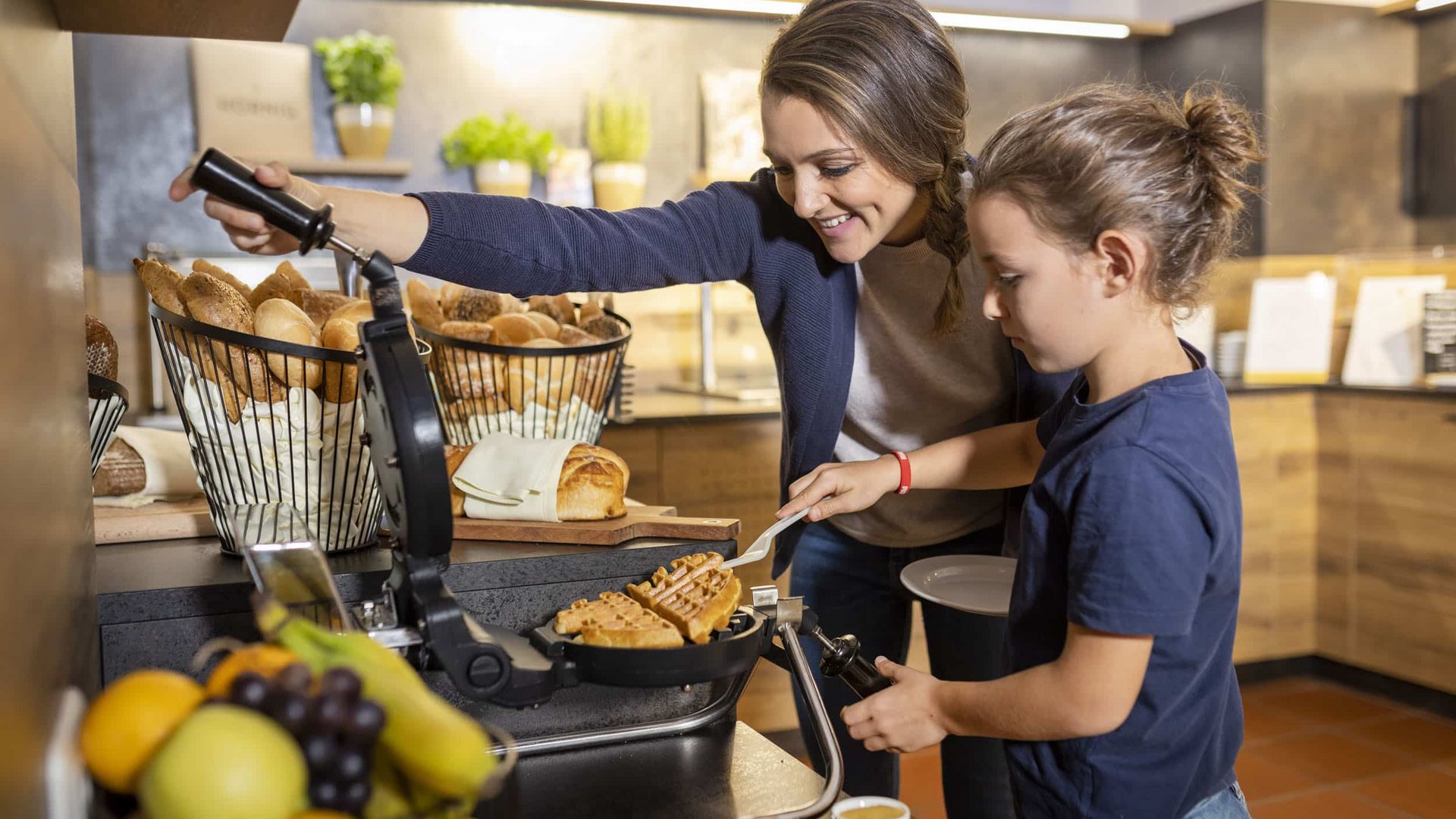 Woman and child making waffles with waffle iron in kitchen