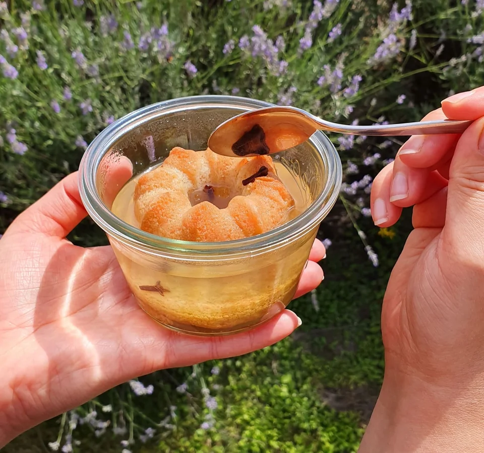 Hand houdt glas met gelei en cake ring, lepel raakt gelei
