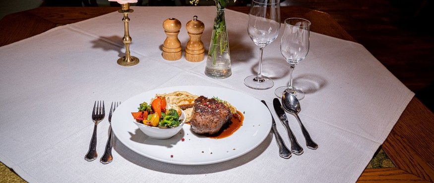 Elegant table setting with steak, vegetables, candlelight, and flower bouquet