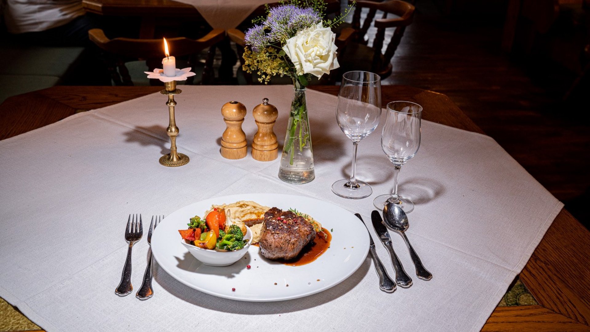 Elegant table setting with steak, vegetables, candlelight, and flower bouquet