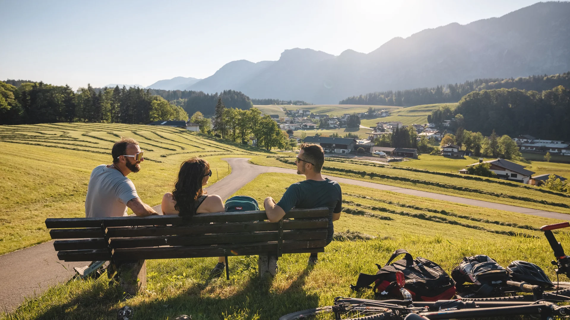 Drei Personen sitzen auf einer Bank mit Fahrrad und Blick auf Landschaft