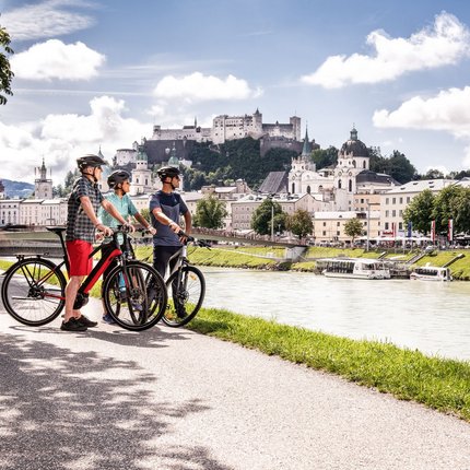 Three cyclists with helmets by riverside near castle and city