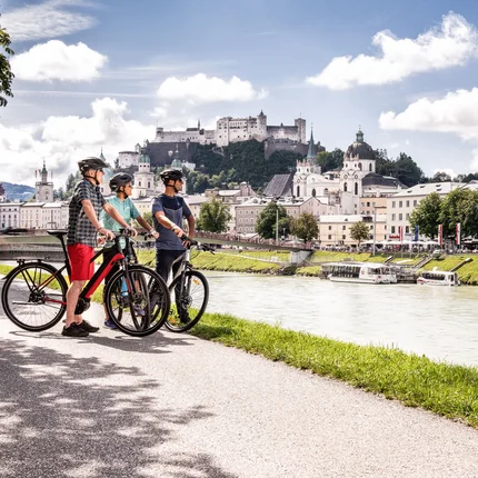 Drie fietsers met helmen bij de rivier naast kasteel en stad