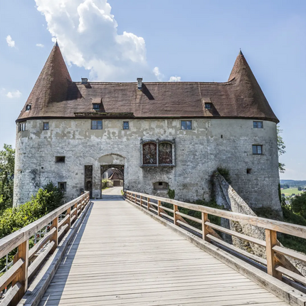 Wooden bridge leading to old stone building with pointed roofs under clear sky