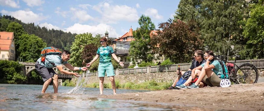 Vier Personen genießen an einem sonnigen Tag einen Fluss mit Radhelmen und Rucksäcken