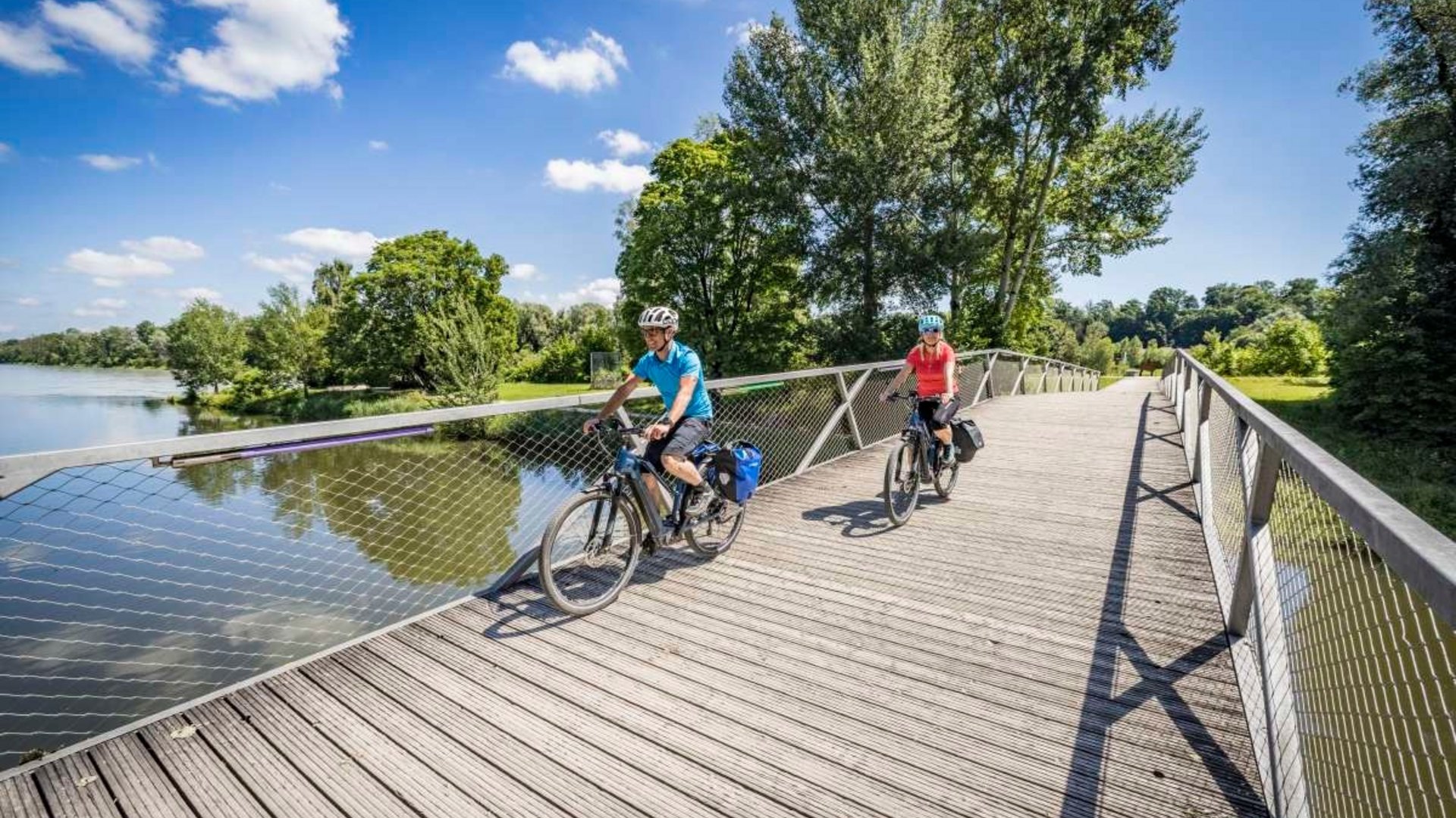 Two cyclists riding on a bridge over a river on a sunny day