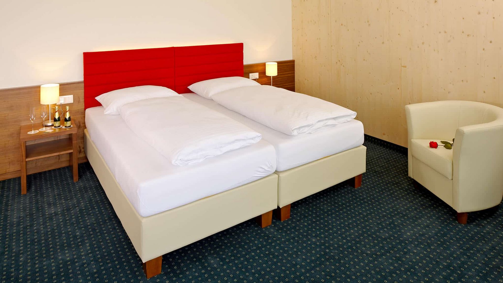 Double bed with red headboard, armchair and nightstand in hotel room