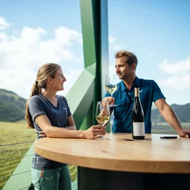 Twee mensen die wijn drinken op een balkon met uitzicht op een wijngaard