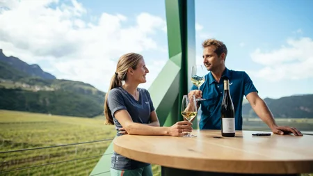 Kulinarisch unterwegs in Tramin © IDM Südtirol - Benjamin Pfitscher Zwei Personen genießen Wein auf einem Balkon mit Blick auf einen Weinberg