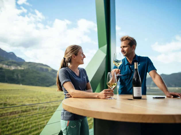 Kulinarisch unterwegs in Tramin © IDM Südtirol - Benjamin Pfitscher Zwei Personen genießen Wein auf einem Balkon mit Blick auf einen Weinberg