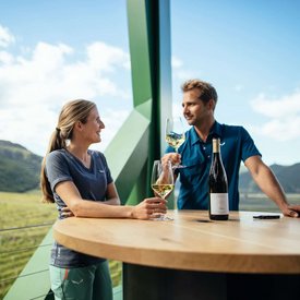 Two people enjoying wine on a balcony overlooking a vineyard