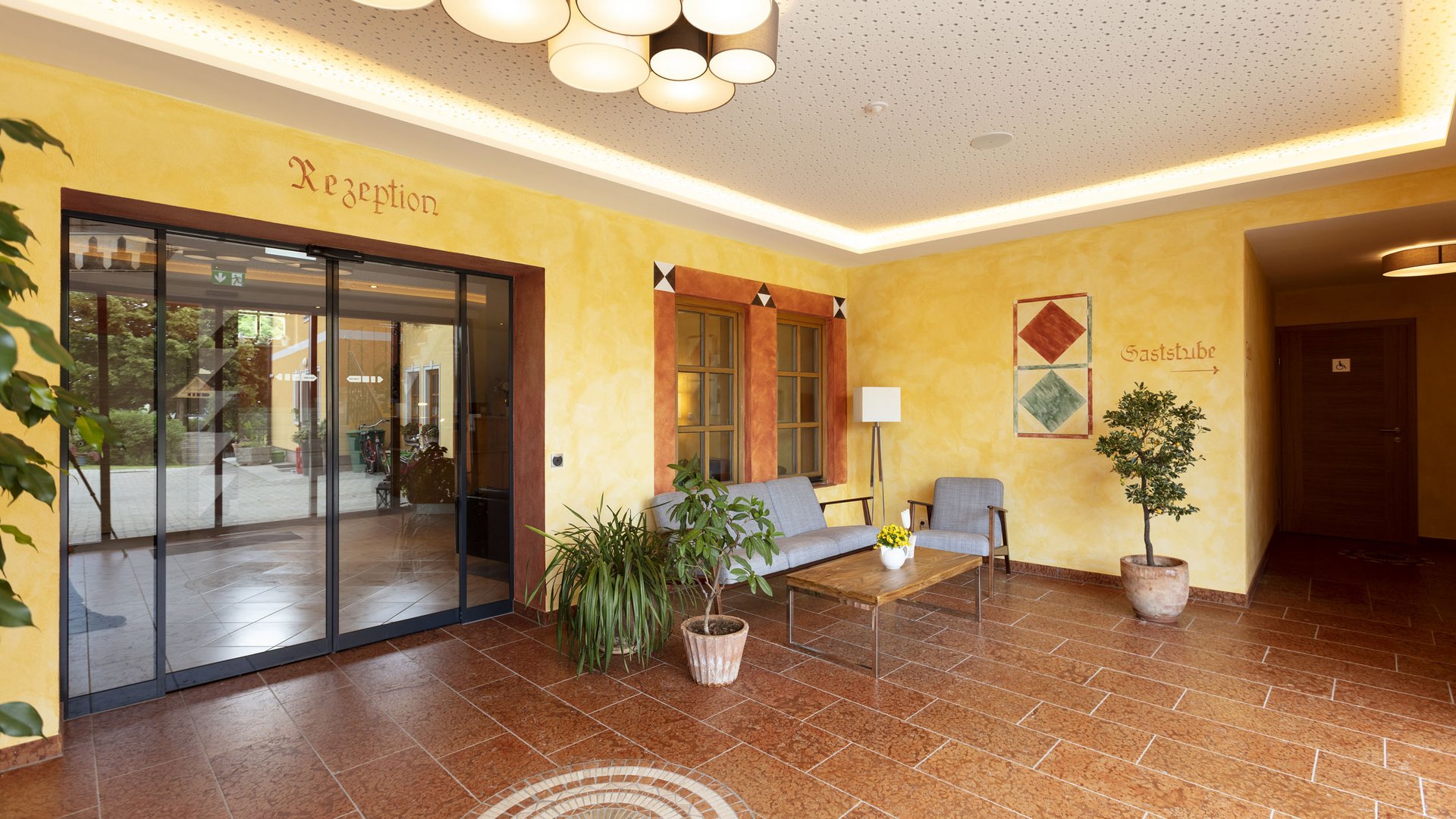 Bright hotel lobby with yellow walls, plants, and seating area