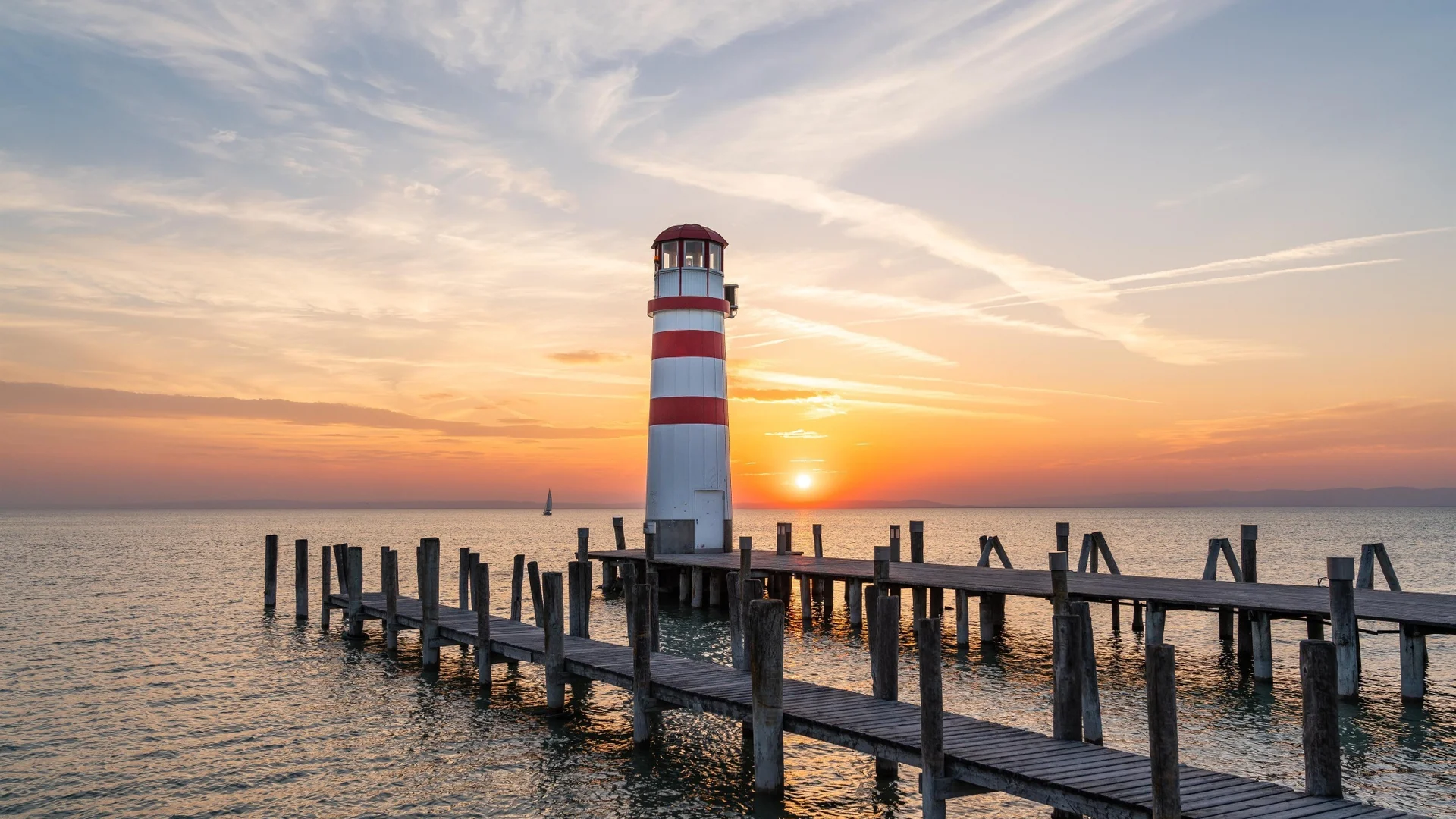 Lighthouse on wooden pier at sunset over the sea