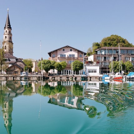 Church tower, houses, and boats reflected in clear lake water