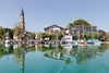 Collective enquiries Church tower, houses, and boats reflected in clear lake water