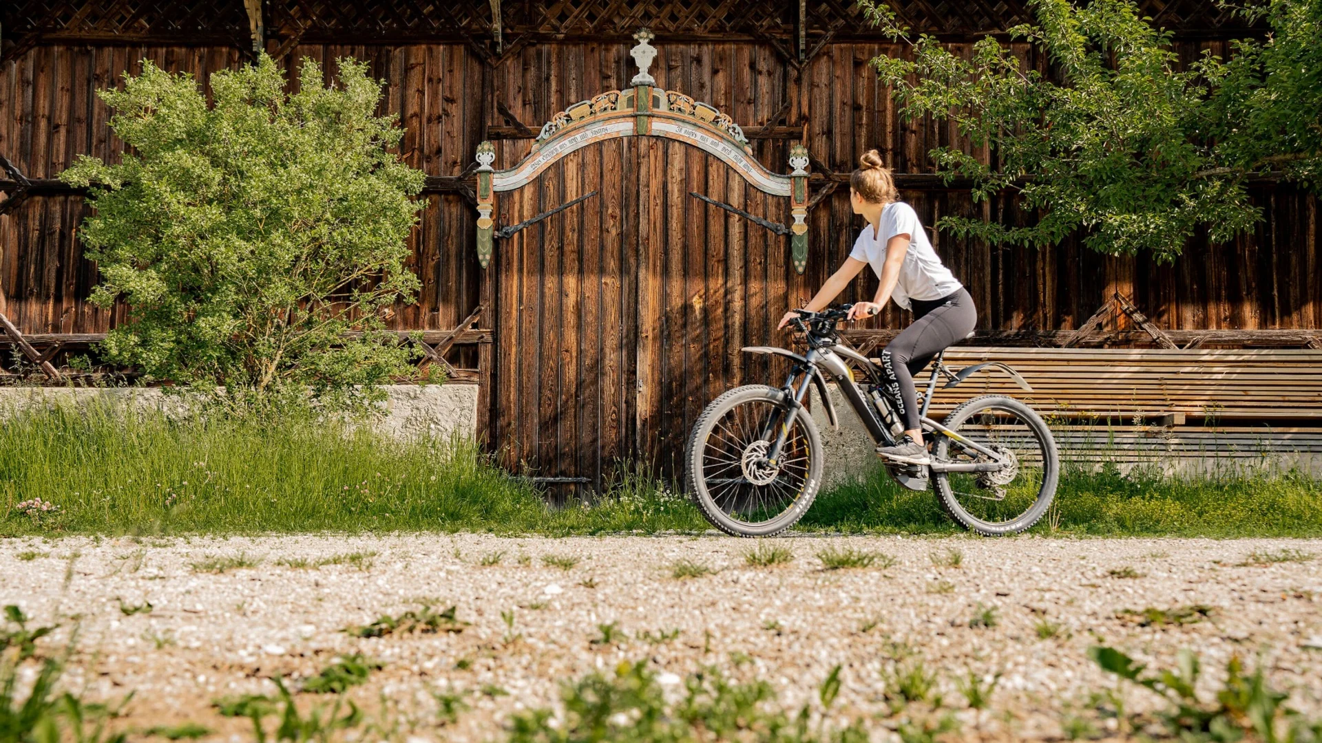 Frau auf Fahrrad vor altem Holztor mit Bäumen