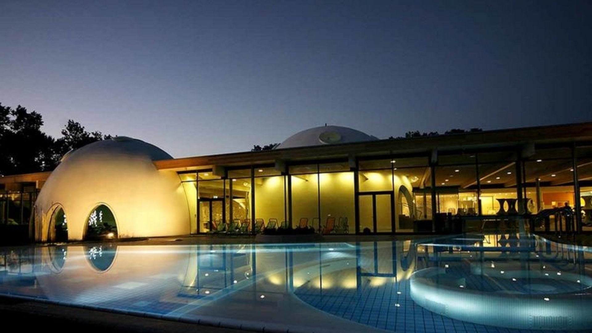 Illuminated swimming pool and building with round white domes at night
