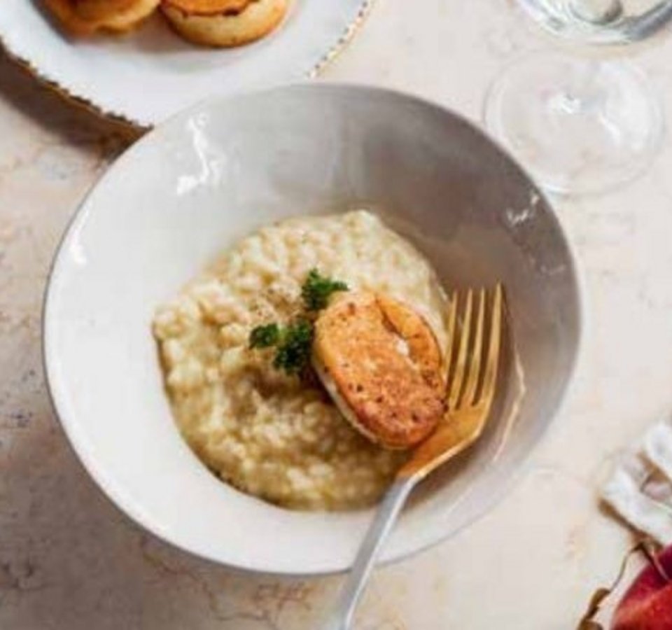 Bowl of risotto with grilled chicken, plate with bread, glass and apple