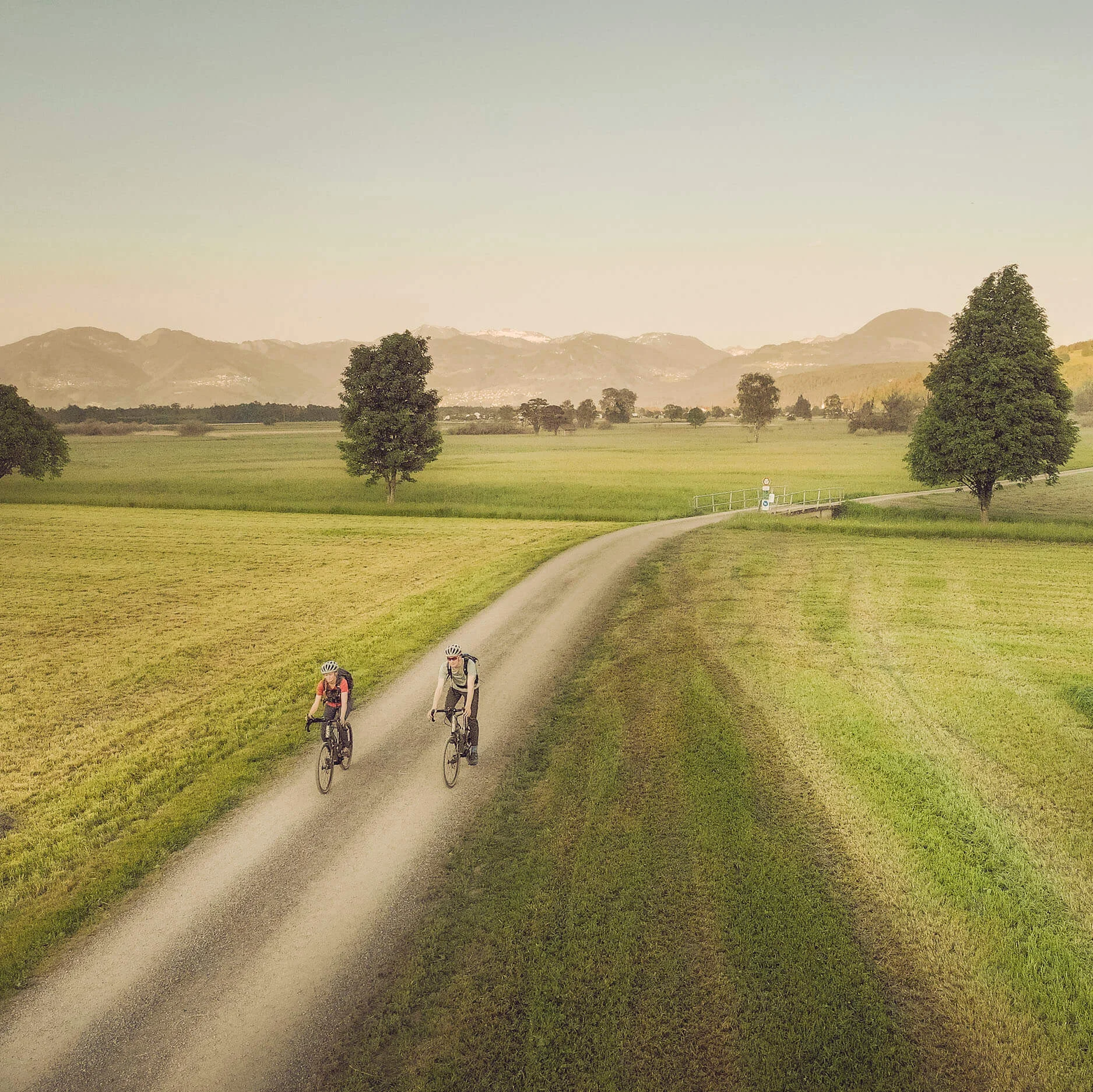 Zwei Radfahrer auf Landweg in grüner Landschaft mit Bergen im Hintergrund