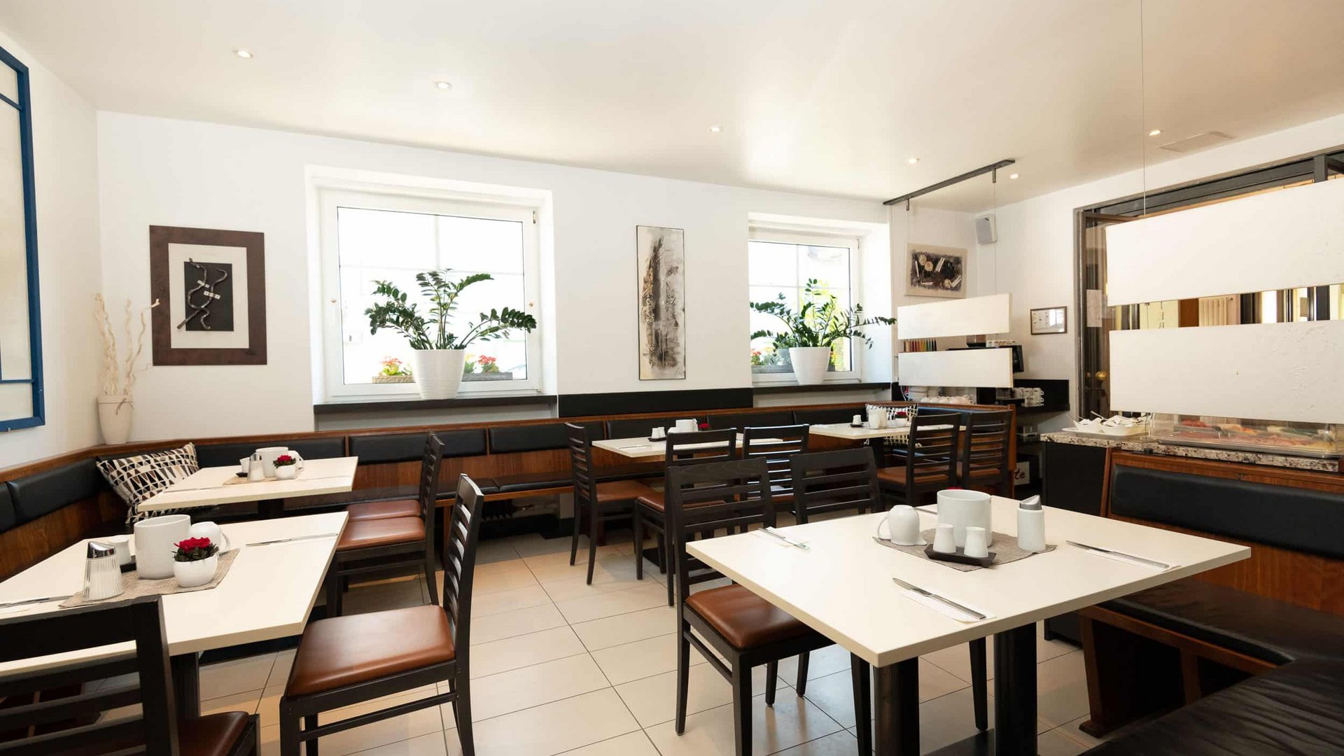 Cozy bright dining area with tables, chairs, and plants on the windowsills