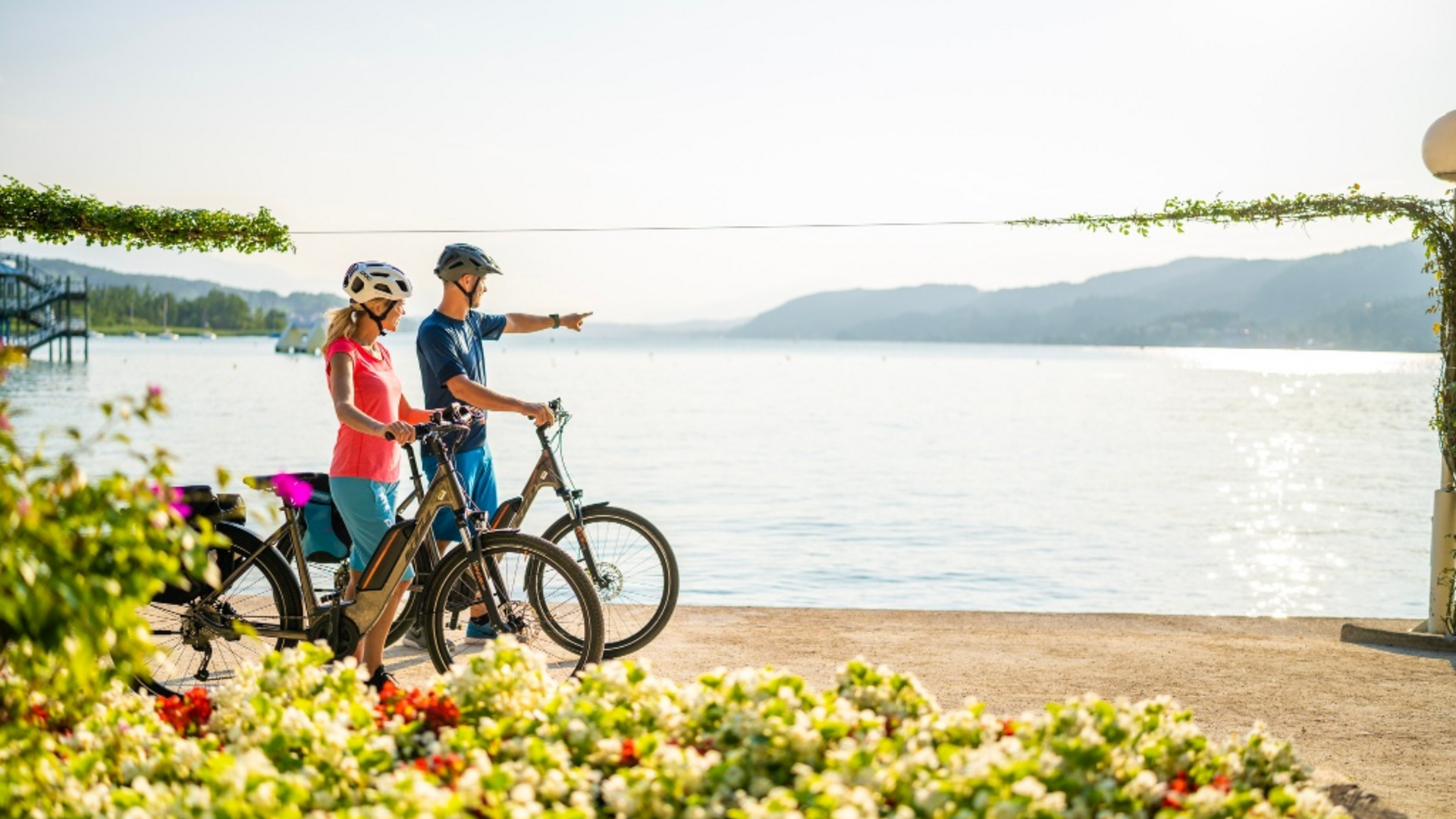 Two cyclists by a lake, one pointing into the distance on a sunny day