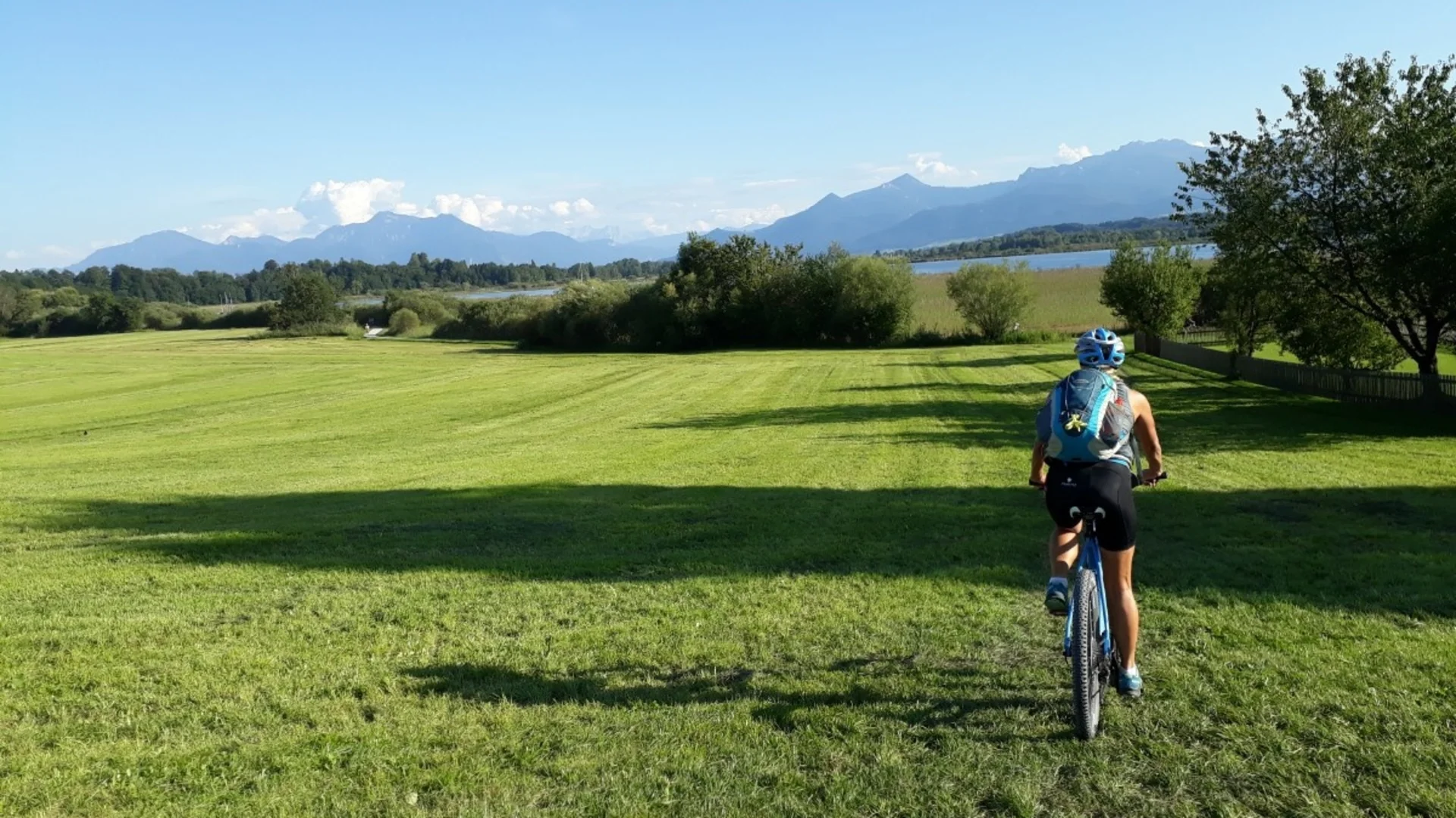 Cyclist riding across green field with mountains in the background