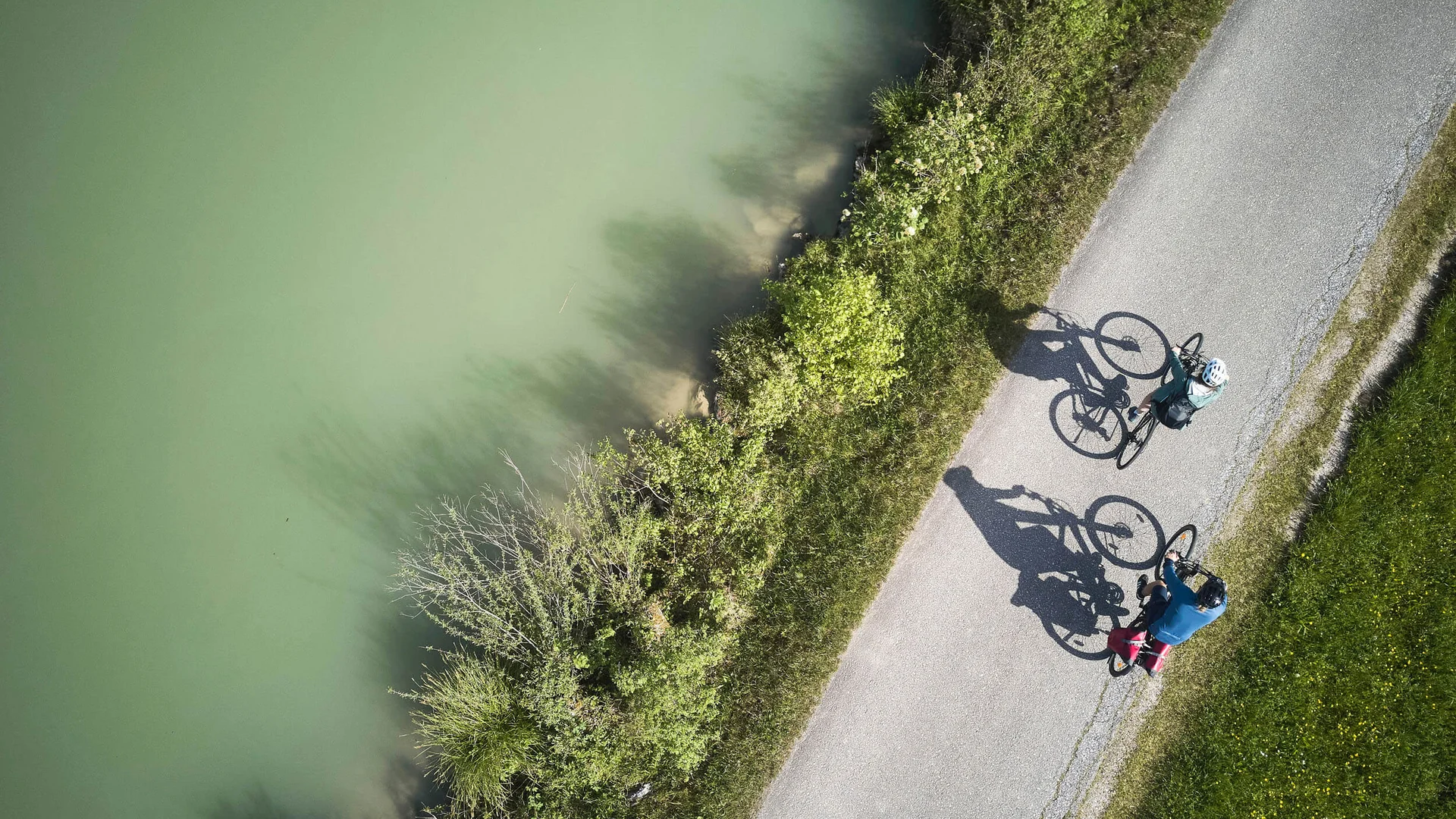 Zwei Radfahrer auf einem Weg neben grünem Wasser und Vegetation