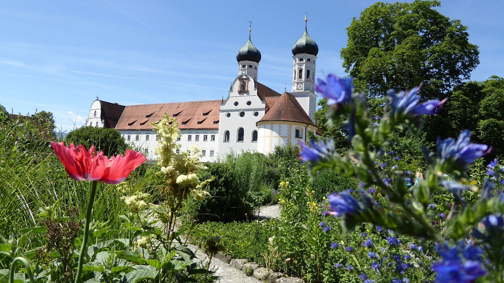 Klostergarten mit bunten Blumen und Kirche im Hintergrund bei Sonnenschein