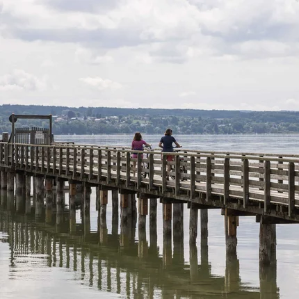 Zwei Radfahrer auf einem langen Holzsteg über ruhigem Wasser