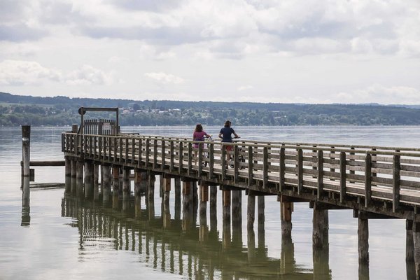 Two cyclists on a long wooden pier over calm water