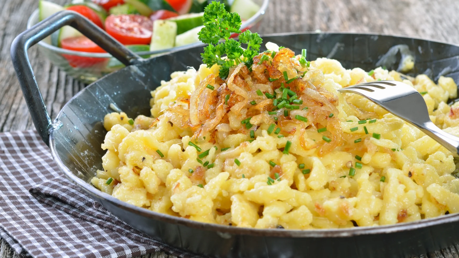Käsespätzle mit Röstzwiebeln und Petersilie in Pfanne mit Gurken-Tomatensalat