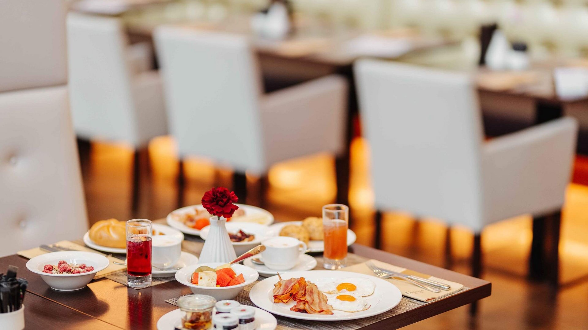 Breakfast with eggs, bacon, fruit, and drinks on set table in restaurant