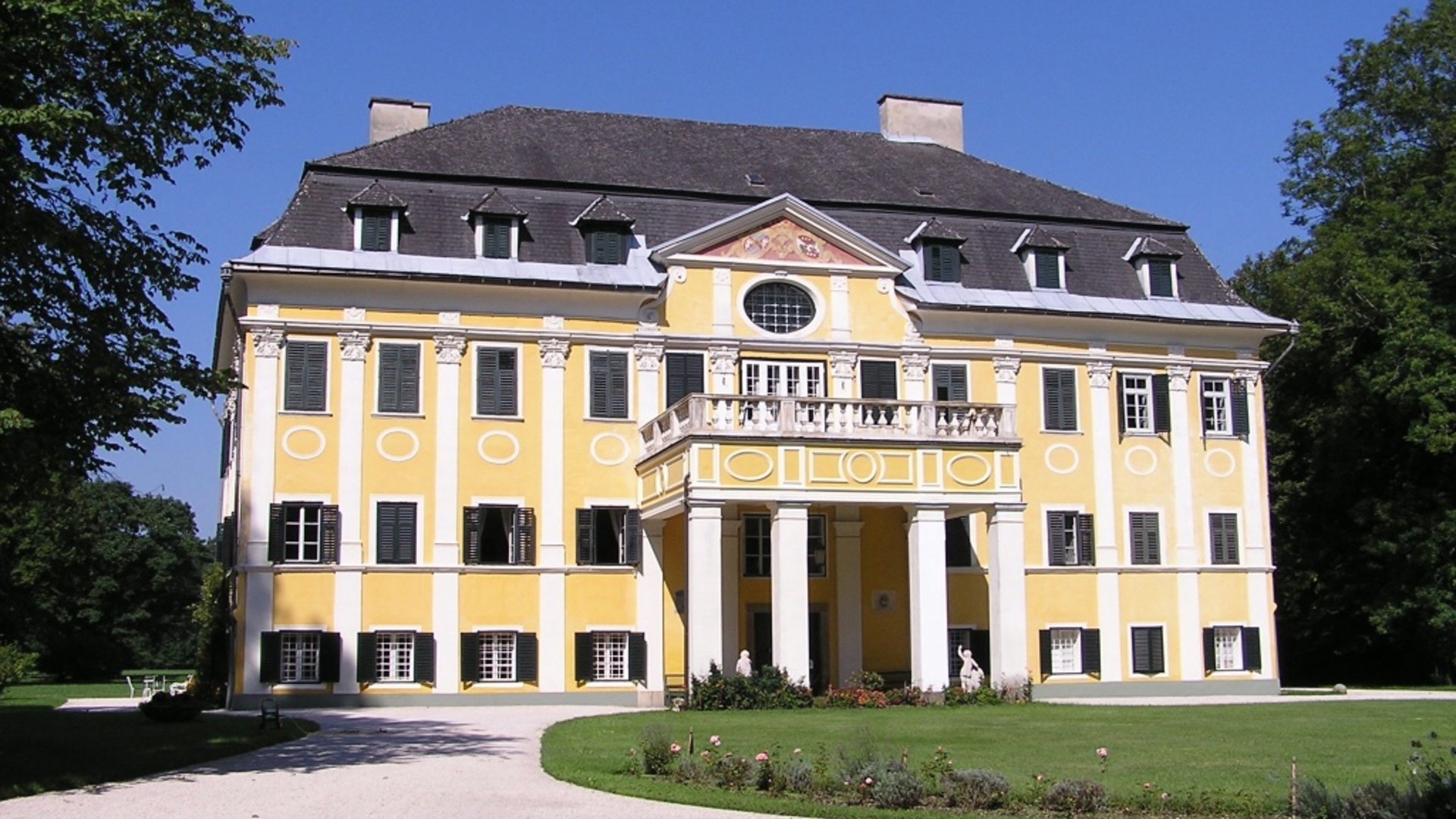 Yellow manor house with columns and round window under clear sky