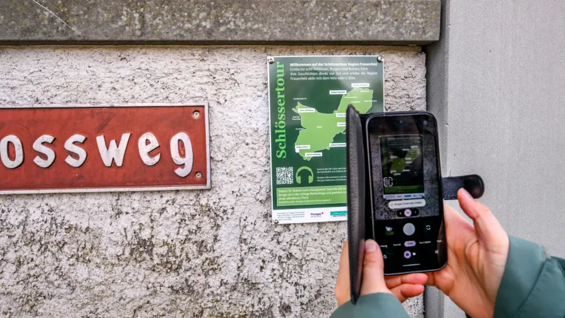 Tour-Detail © Balz Kubli Person scannt eine Infotafel mit einem Smartphone an einer Außenwand