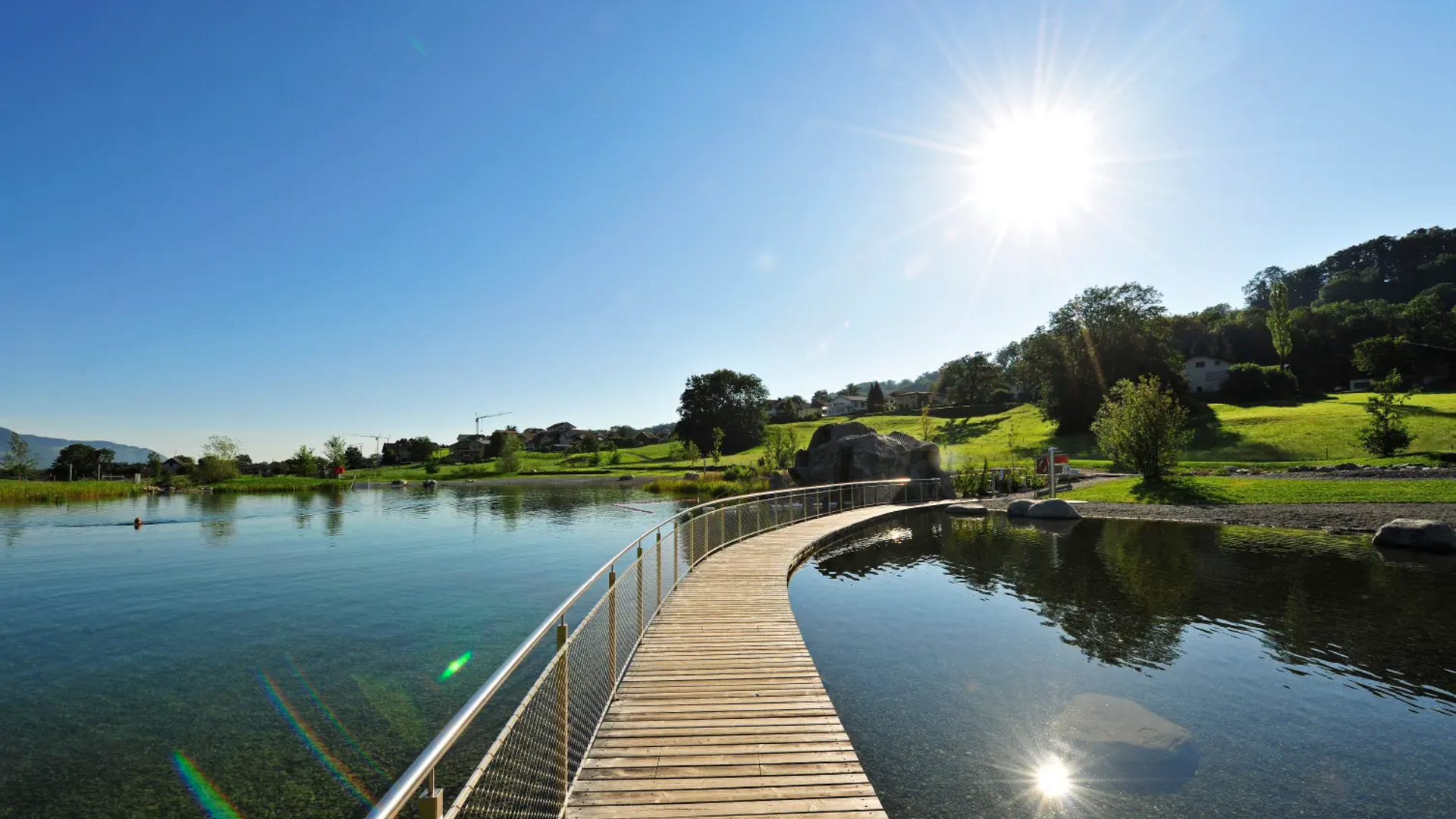 Wooden walkway over calm lake under clear blue sky with bright sun