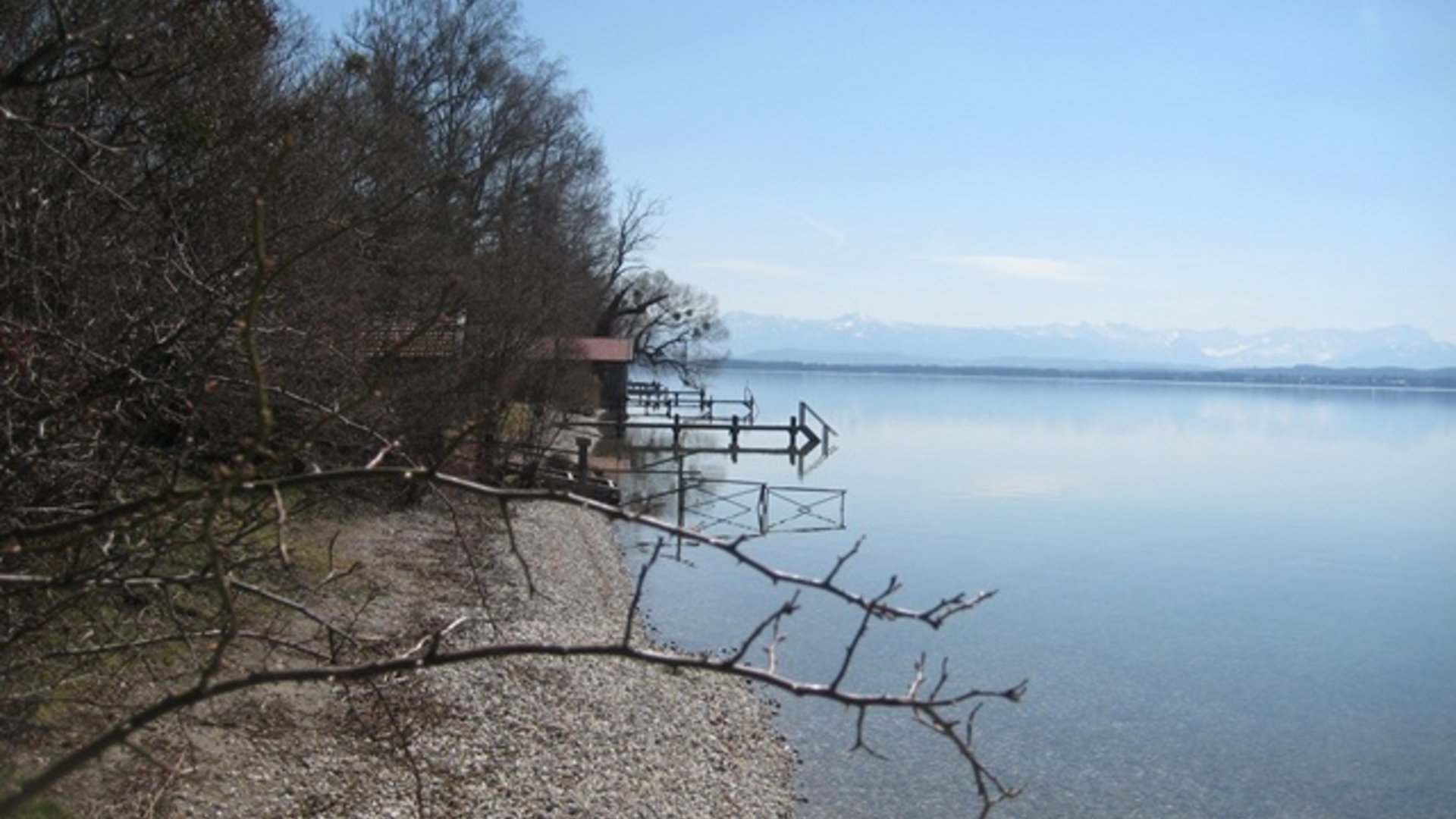 Rocky lakeshore with bare trees and mountains in the distance