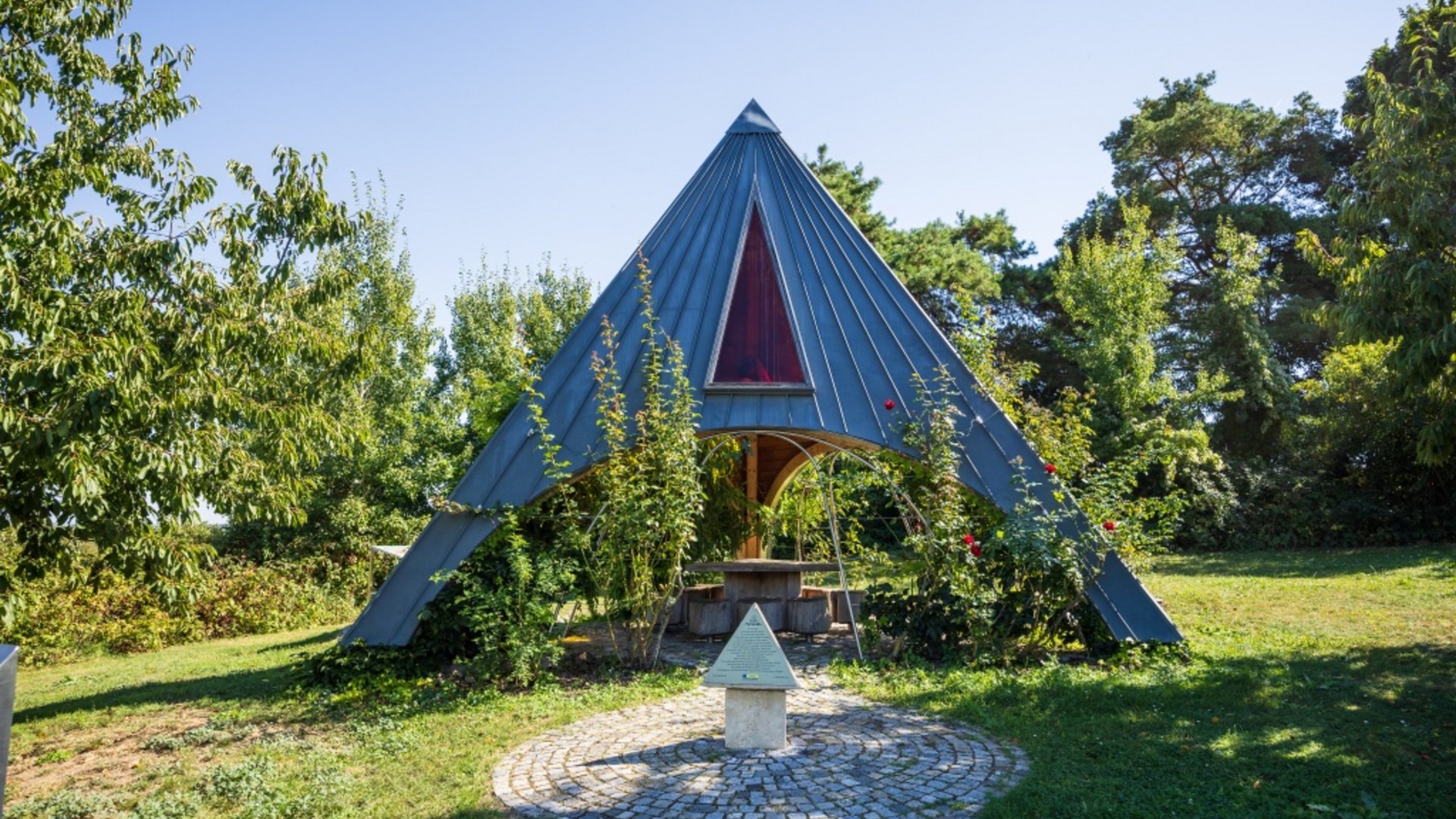 Pavilion with pointed roof surrounded by trees in a garden