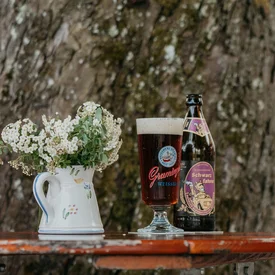 Bierfles en gevuld glas op houten tafel naast boom in biergarten