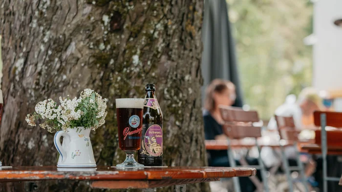 Bierflasche und gefülltes Bierglas auf Holztisch neben Baum im Biergarten
