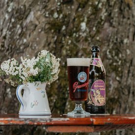 Beer bottle and filled glass on wooden table next to tree in beer garden