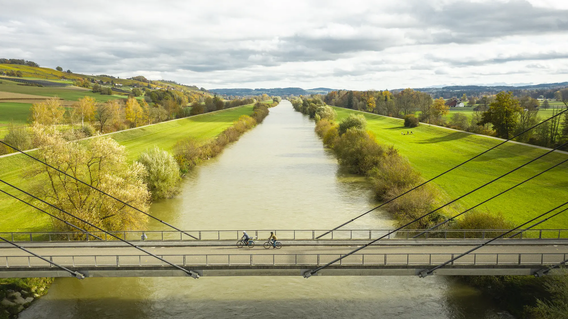 Two cyclists on a bridge over a river in a green landscape