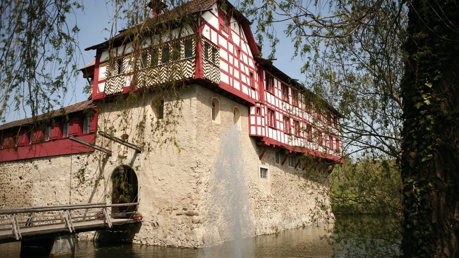 Historic timber-framed house by water with fountain and old wooden bridge
