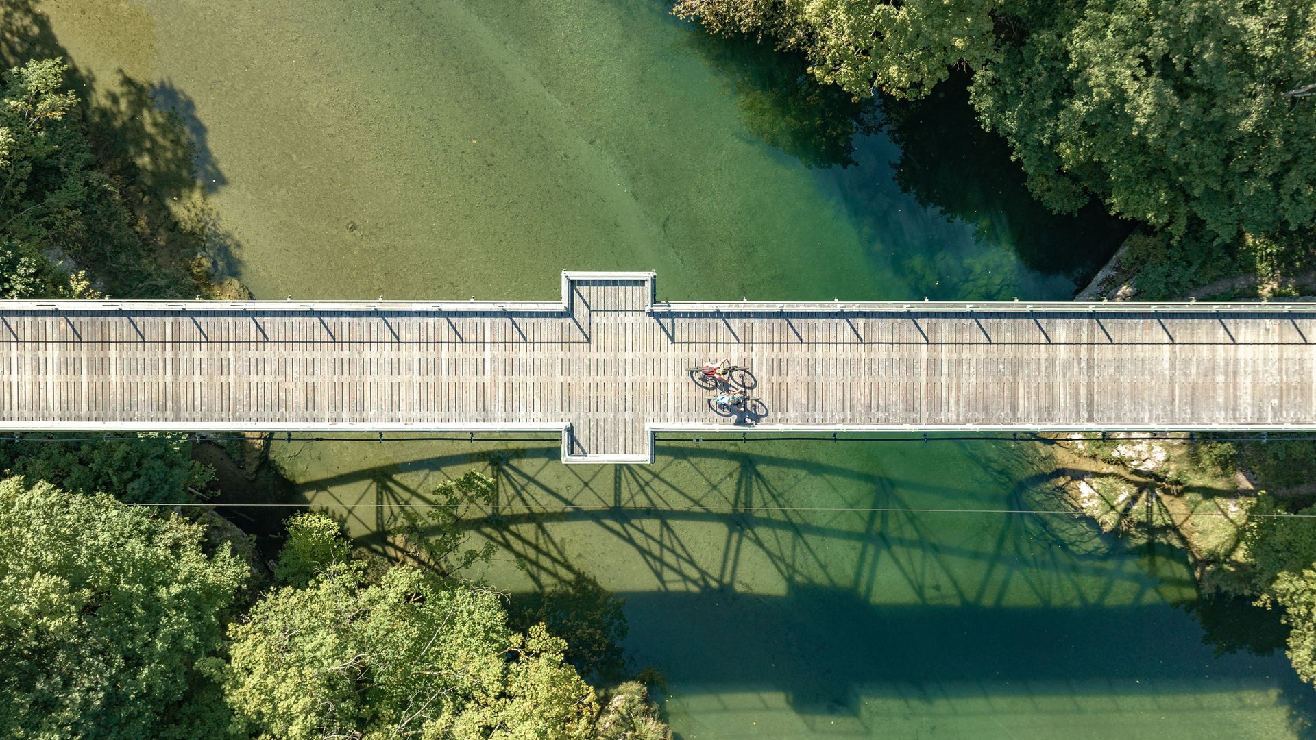 Aerial view of a wooden bridge over green water with two cyclists